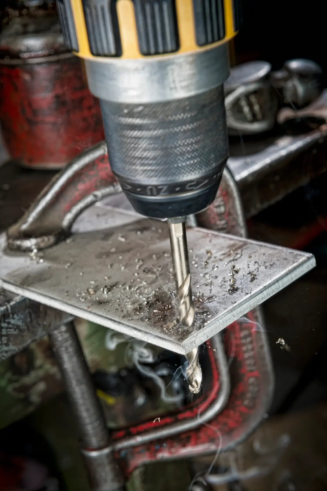 A DEWALT drill bit drilling into a metal sheet held by a clamp, with metal shavings visible.