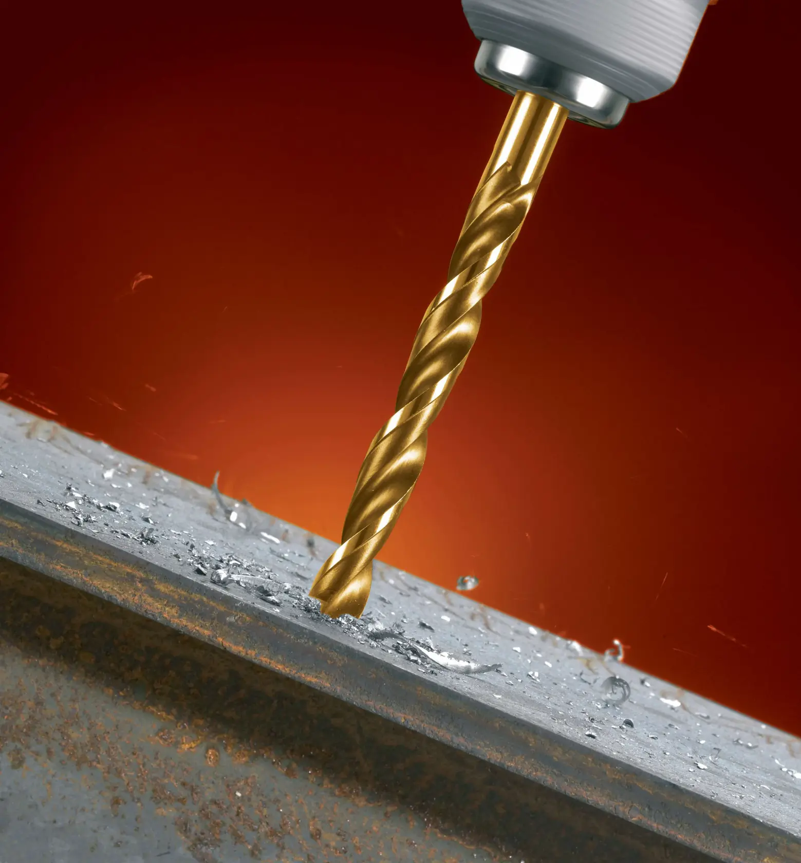 Primer plano de una broca dorada acoplada a un taladro, perforando una pieza de metal con virutas de metal visibles alrededor del agujero.