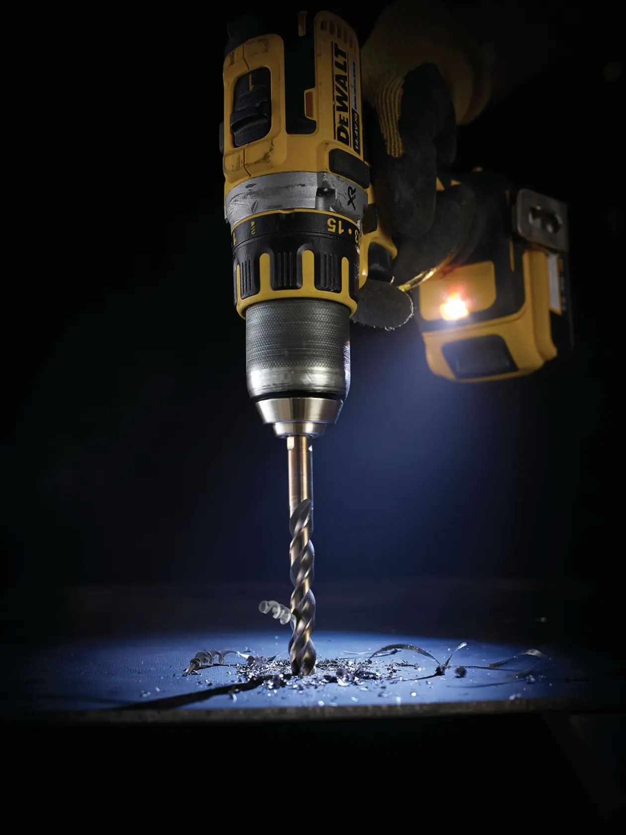 Taladro DEWALT perforando metal, iluminado por luz integrada sobre una superficie oscura.