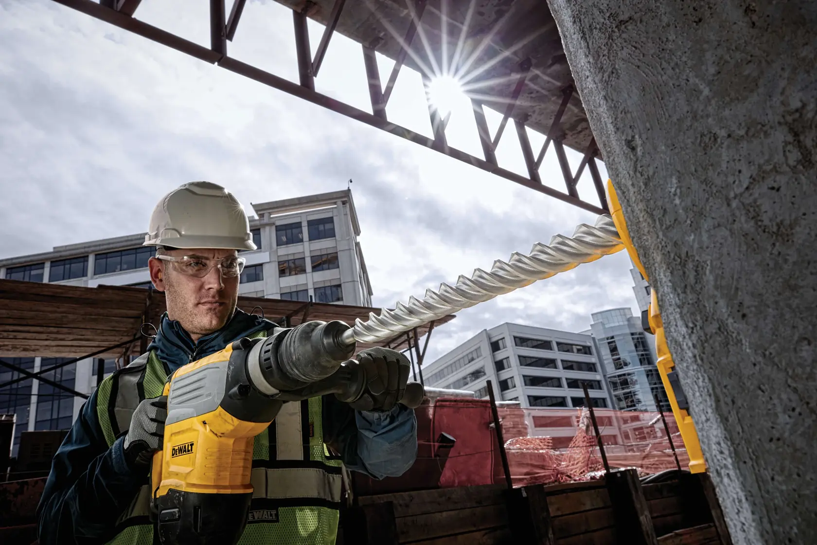 Trabajador usa taladro DEWALT con broca DT60811 en obra, edificios al fondo.