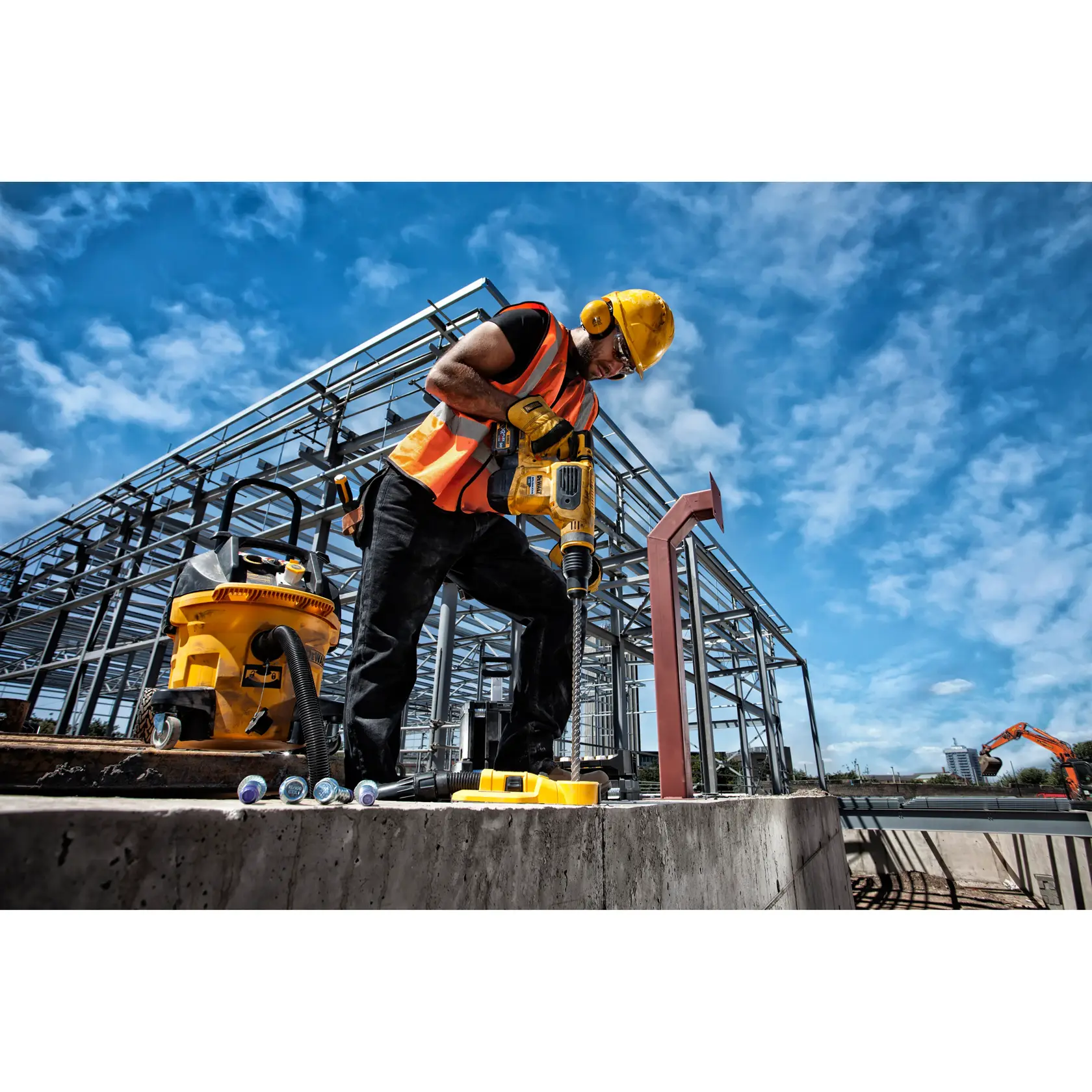 Trabajador usa taladro DEWALT en obra con estructura de acero y cielo azul al fondo.