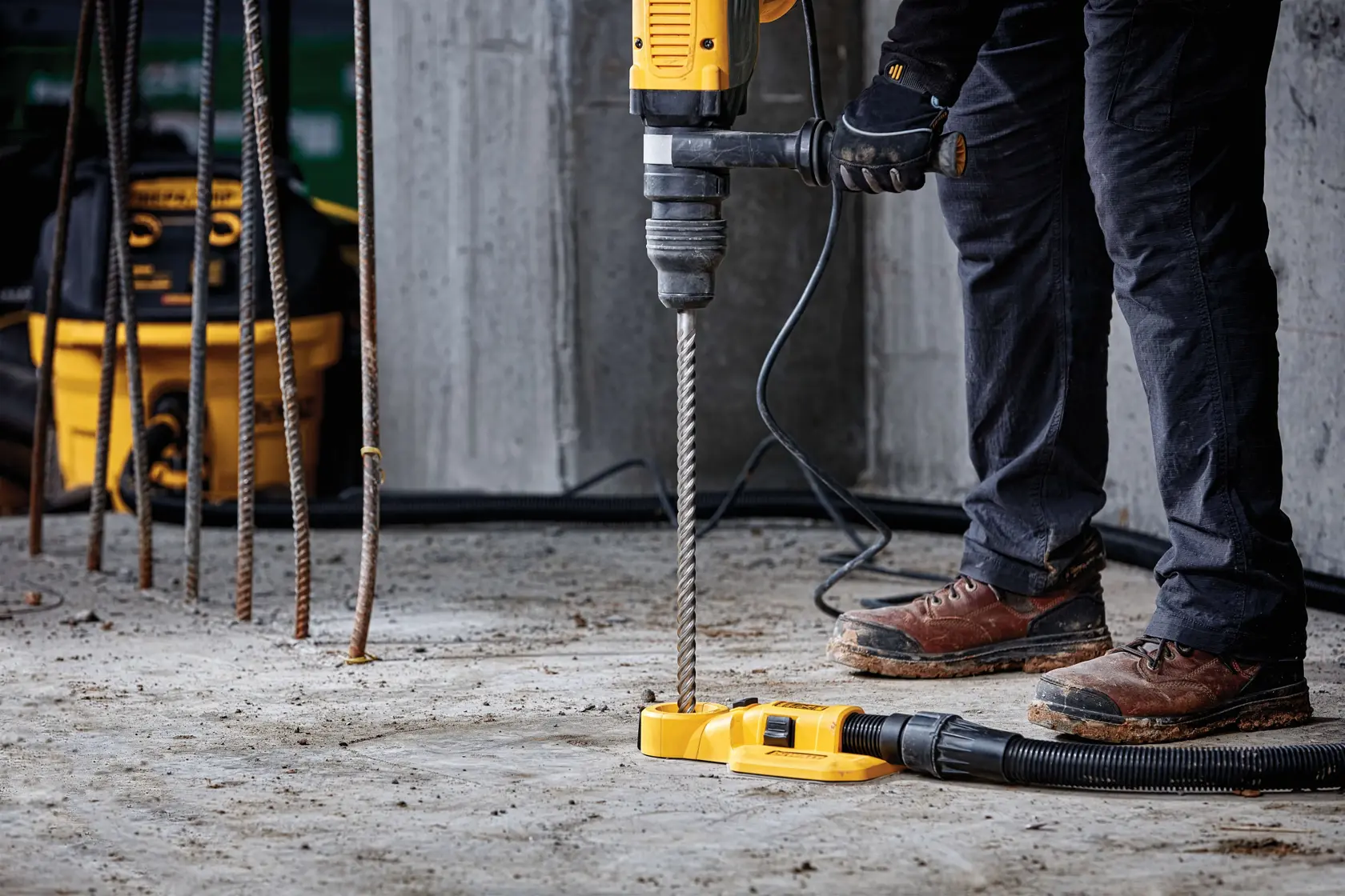 Persona usando taladro DEWALT y extractor de polvo sobre piso de concreto en obra.