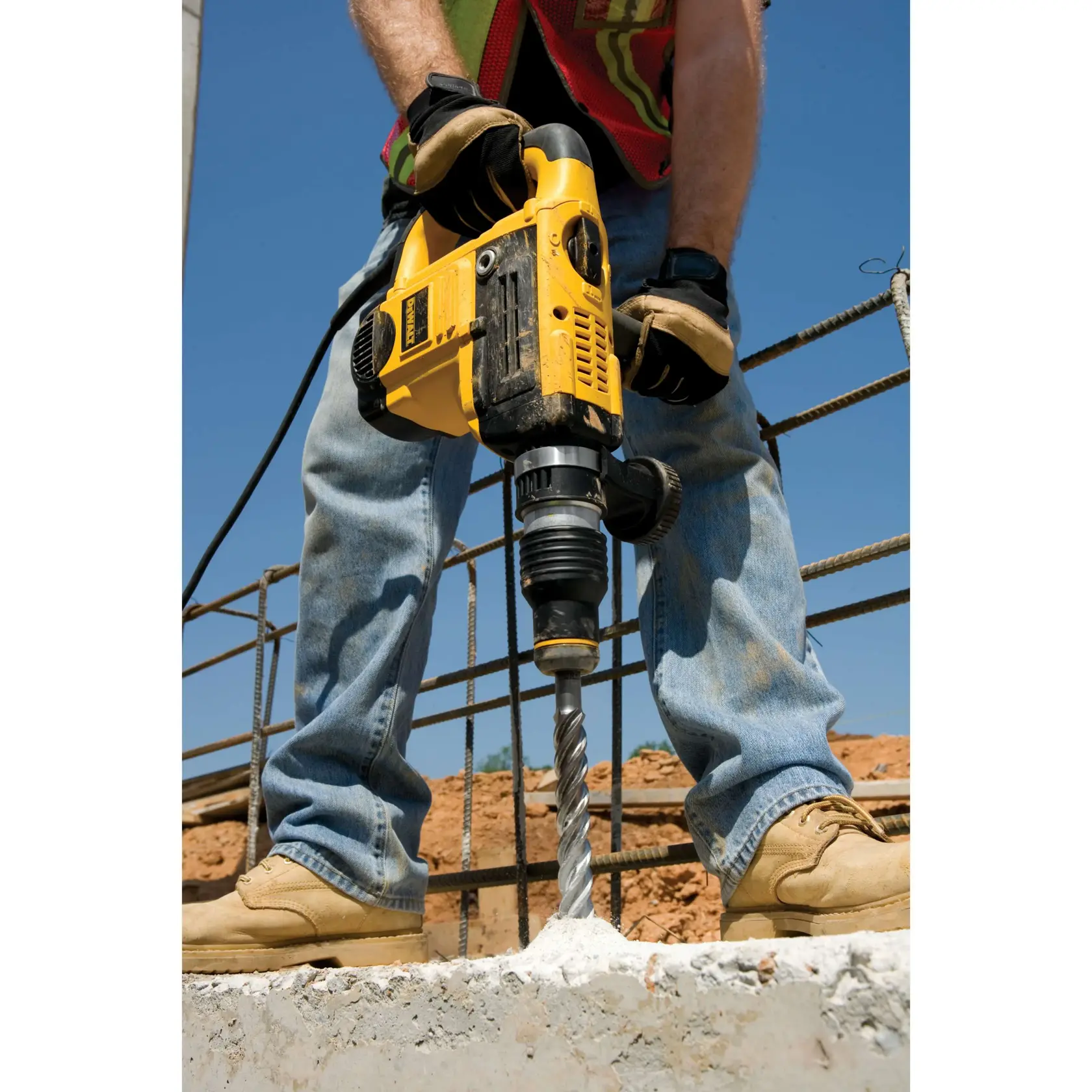 Persona perfora concreto con herramienta DEWALT amarilla en obra, usando guantes y botas de trabajo.