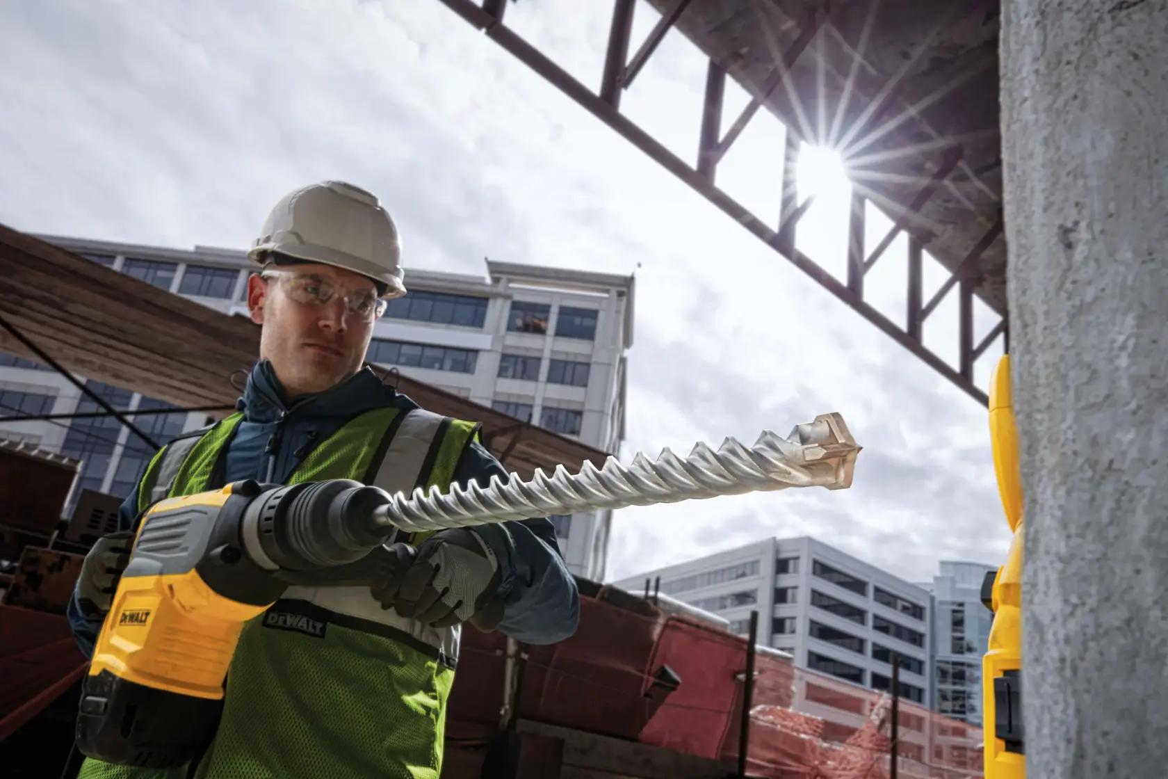 Persona con martillo rotativo DEWALT DT60846 y broca espiral en obra, edificios al fondo.