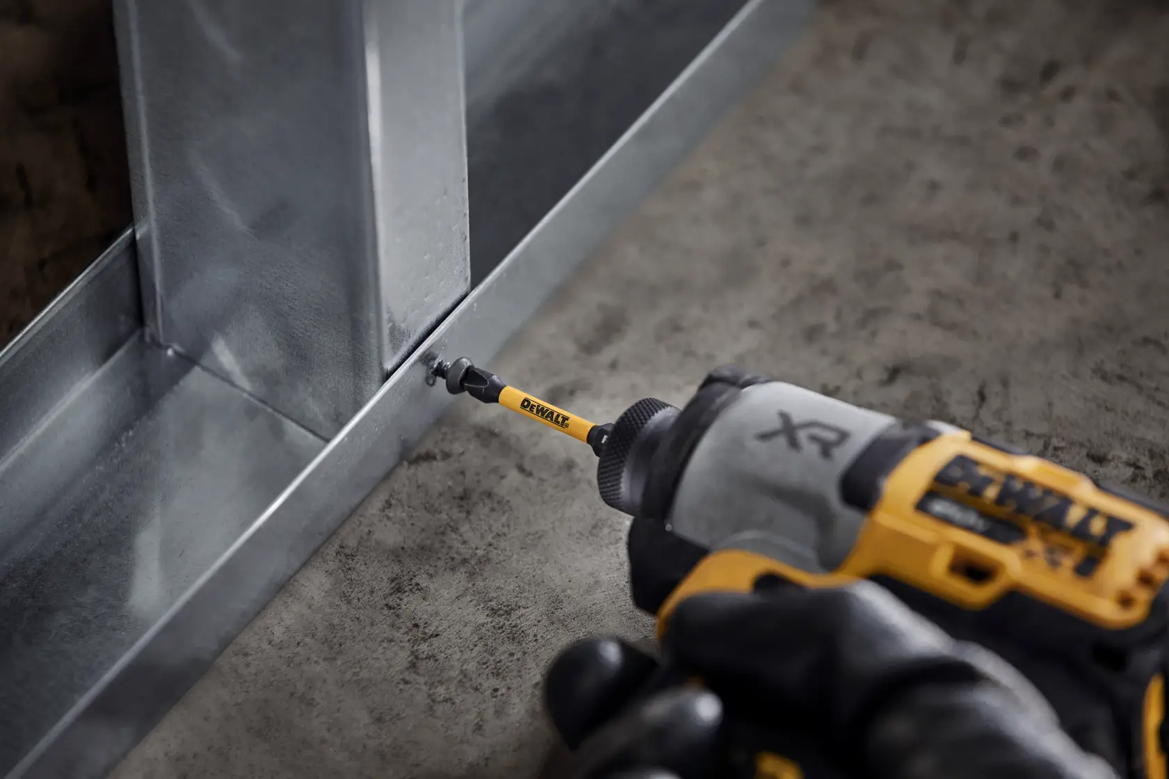 Taladro DEWALT XR atornilla una estructura metálica sobre suelo de cemento, vista cercana de la herramienta.