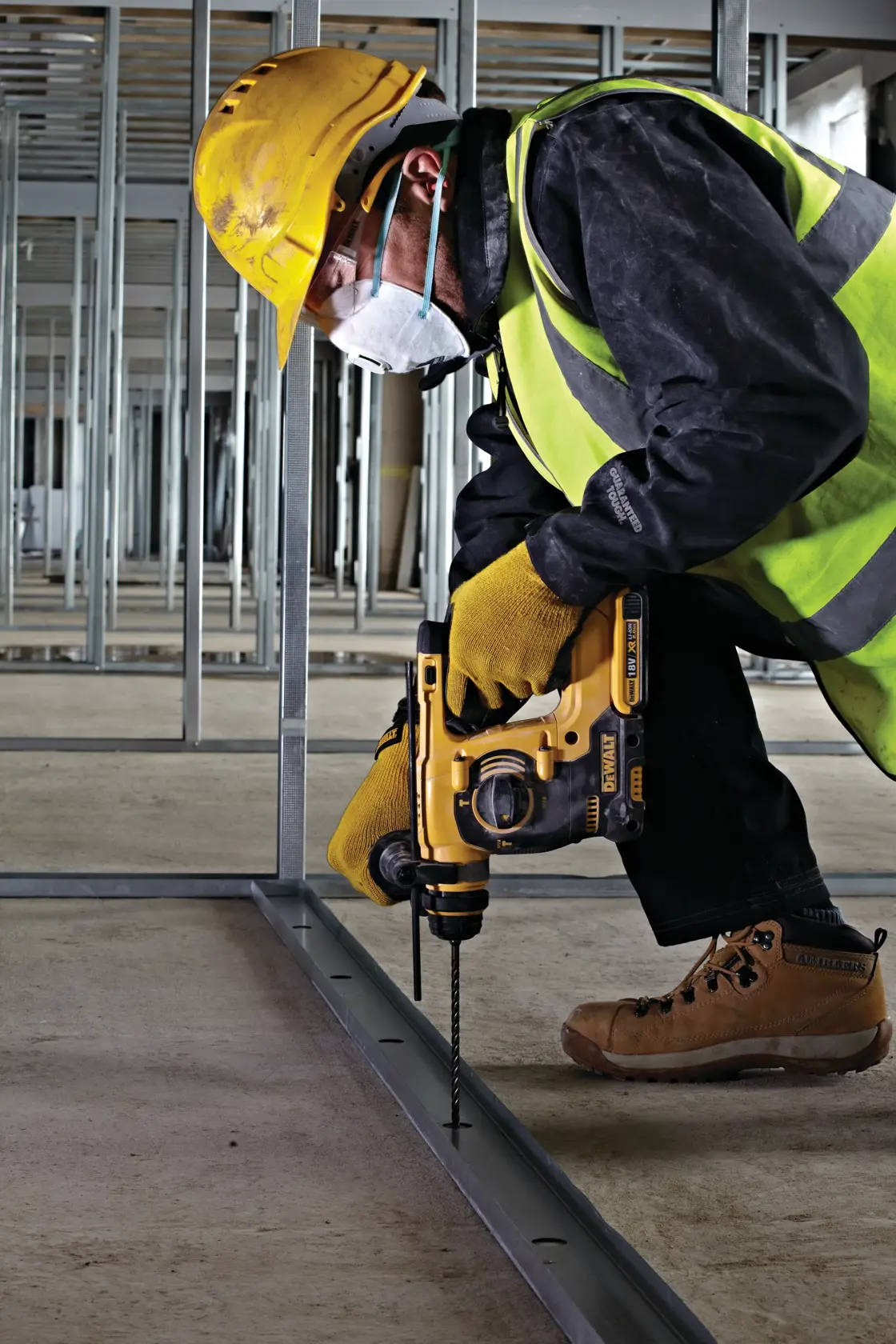 Trabajador usa taladro DEWALT en estructura metálica, con casco, guantes, chaleco y mascarilla en obra.