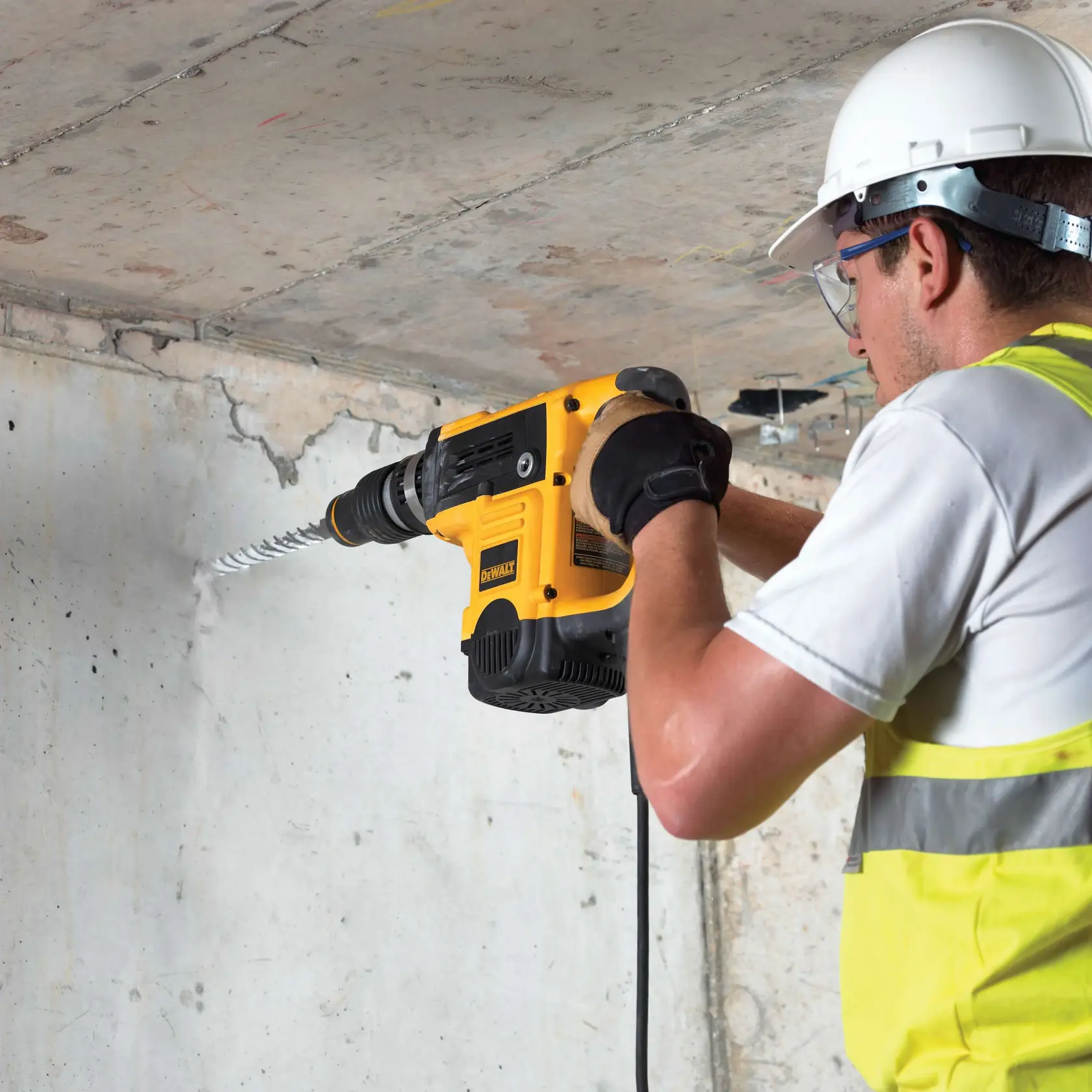 Person bohrt Betonwand mit DEWALT-Bohrhammer. Sicherheitshelm, Handschuhe, Weste.