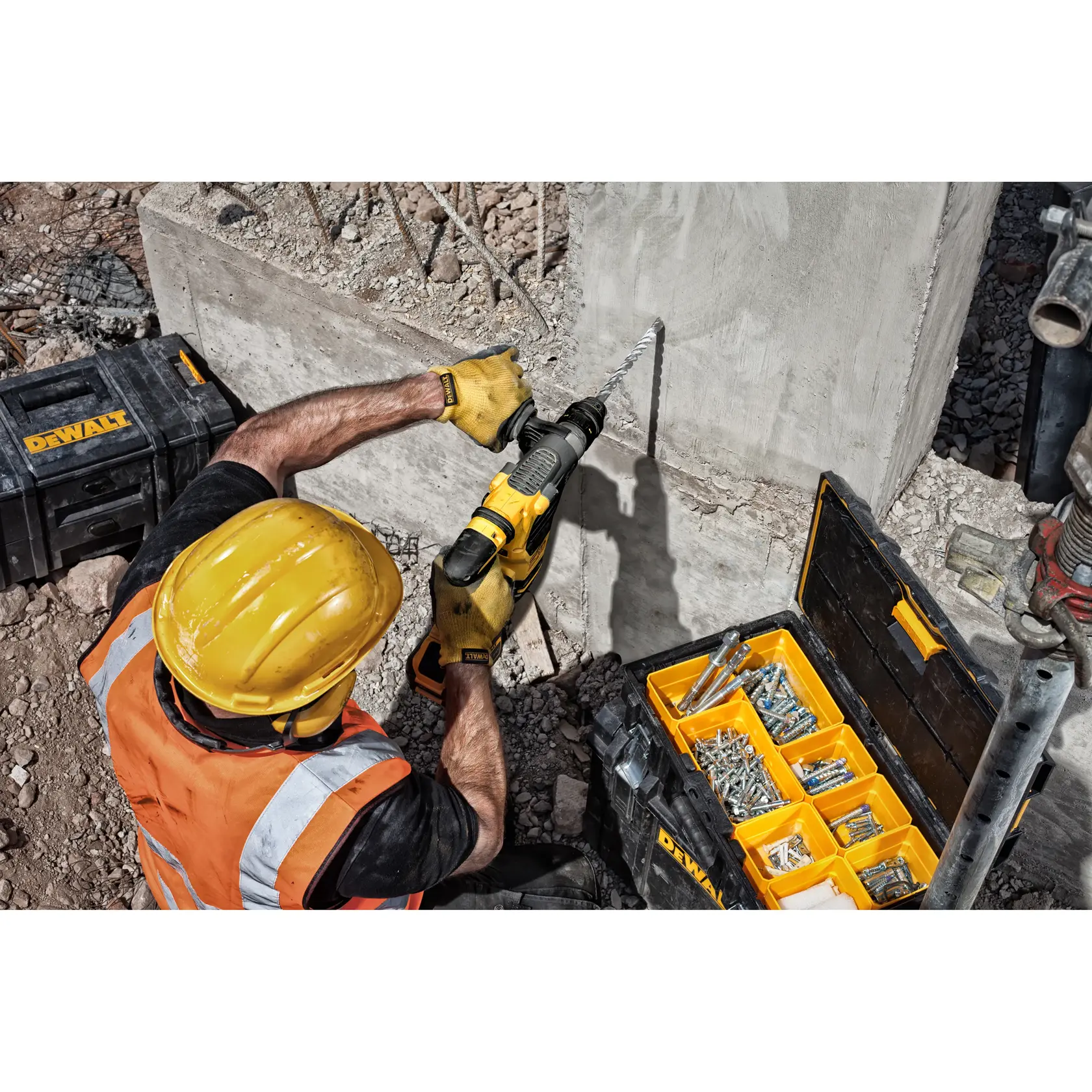 Trabajador usa taladro DEWALT en concreto con protección y caja de herramientas abierta en obra.