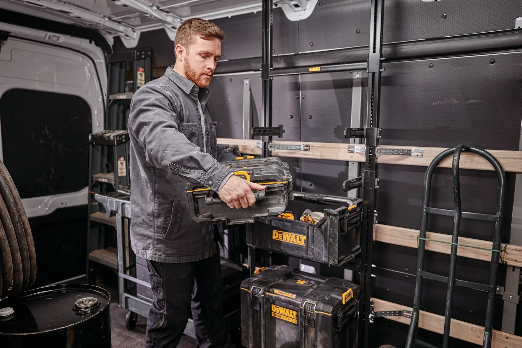 Persona organizando cajas de herramientas DEWALT en una furgoneta con estanterías.
