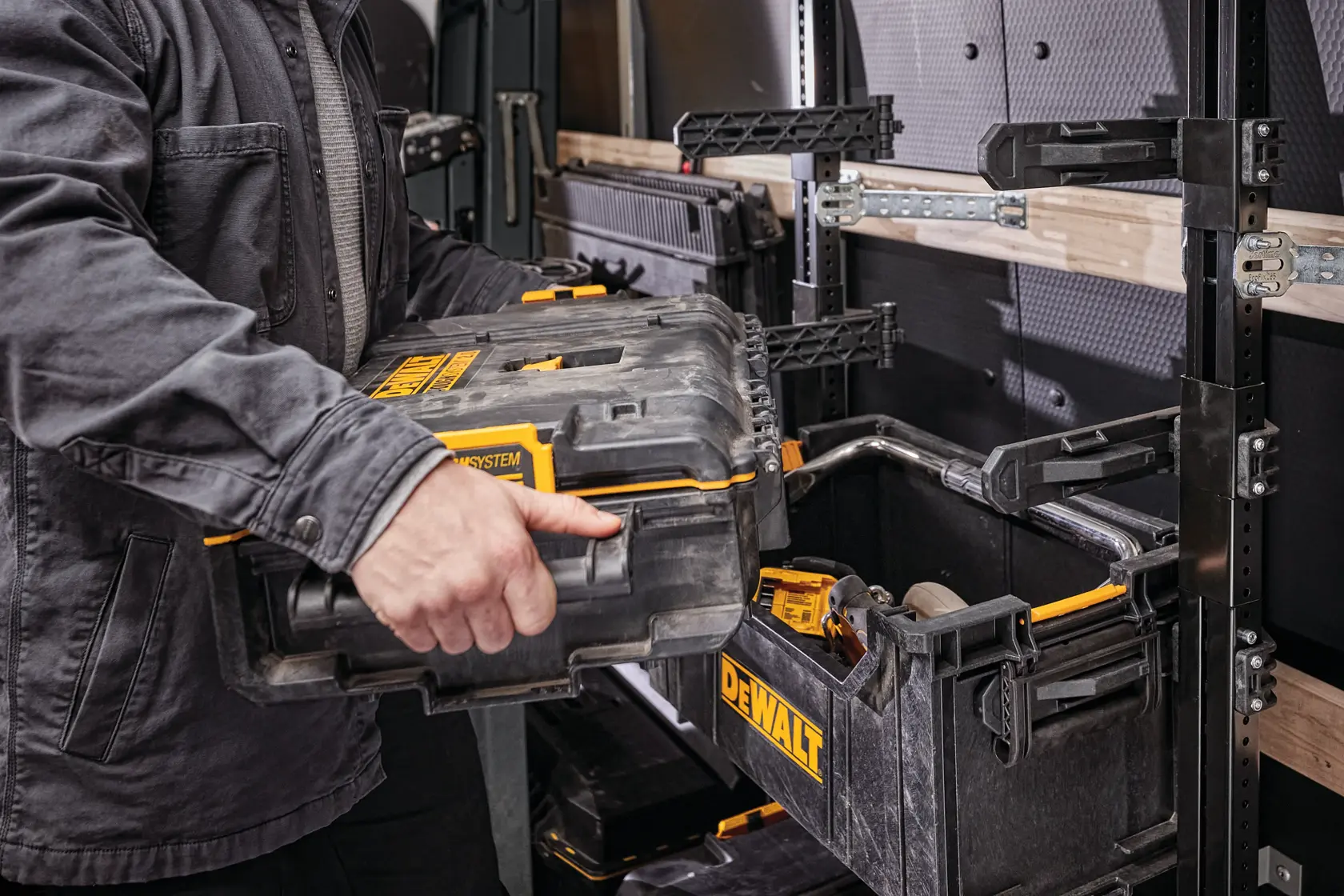 Persona coloca una caja DEWALT en un sistema modular de estantes dentro de taller o vehículo utilitario.